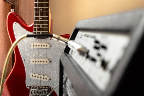 Red electric guitar plugged into large speaker in interior place. Amplifier with blur effect and guitar in the background. Playing guitar in home.