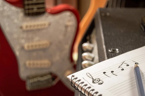 Arka planda gitar ve bas olan bir not defterine müzik bestelemek. Müzik stüdyosunda müzisyen yazısı. Üç katlı anahtarla besteleme.