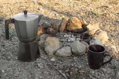 Ormandaki bir kamp sırasında şenlik ateşiyle kahve hazırlamak. Kayalı şenlik ateşi, kahve makinesi moka ve bardak. Yolculuk sırasında kahve hazırlama.