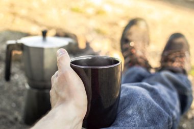 Kahveyi şenlik ateşiyle hazırlamak, kamp sırasında dinlenmek. Birinci şahıs görüşü: şenlik ateşi, yürüyüş botları, kahve makinesi ve sıcak kahve fincanı..
