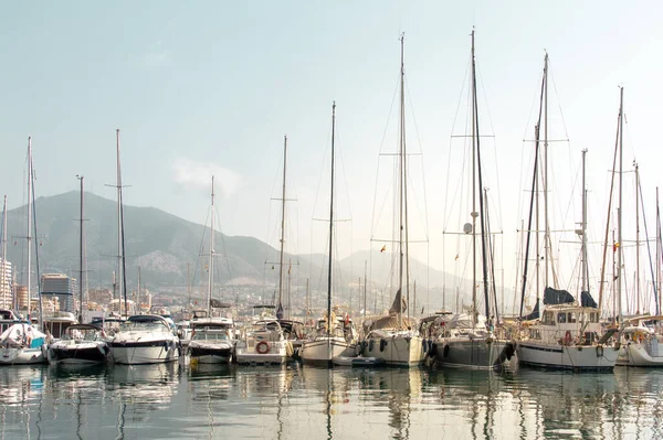 Rıhtımdaki yelkenli ve yatlar şehre ve arka plandaki dağlara yansıdı. Costa del Sol 'un (Fuengirola) manzarası, İspanya.