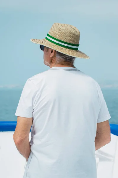 Old man with sunglasses and hat travel by boat during his vacation. Blur background of the sea and blue sky. Old man traveling.