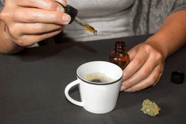 Kahve fincanına CBD tentürü dökmek, marihuana ile yapılan doğal ilaç. Marihuana tomurcuğuyla aynı masada esrar kullanan bir kadın..