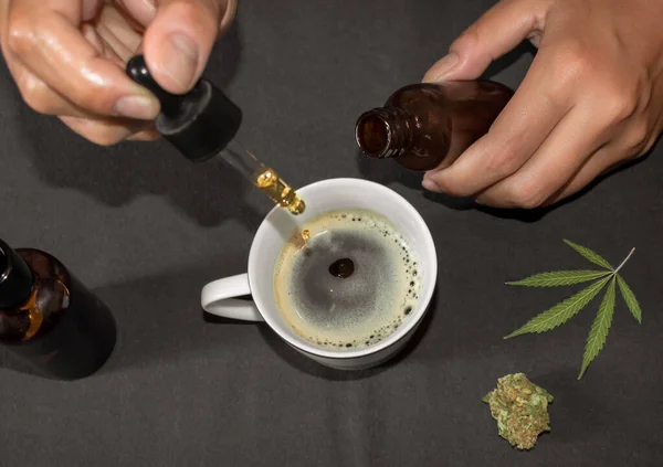 Marihuana 'nın doğal çaresi olarak kahve fincanına CBD tentürü dökmek. Marihuana yaprağıyla dolu bir masada marihuana yağı kullanan kişi..