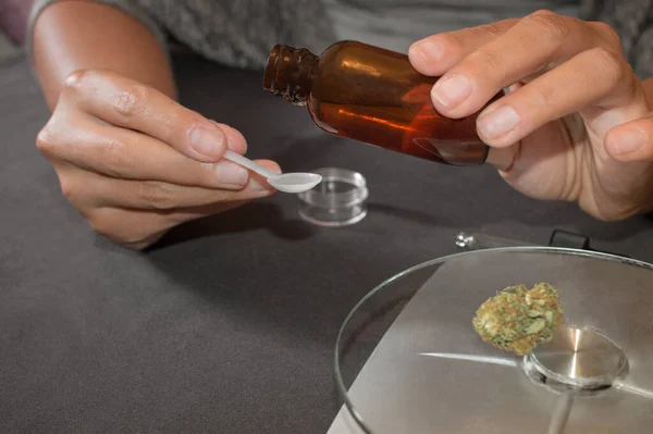 Kadın kendi CBD tentürünü yapıyor. Ağrı için güçlü kenevir özütü. Esrar yağı dozu hesaplanıyor, ağırlığı ve marihuana tomurcuğu olan masa..