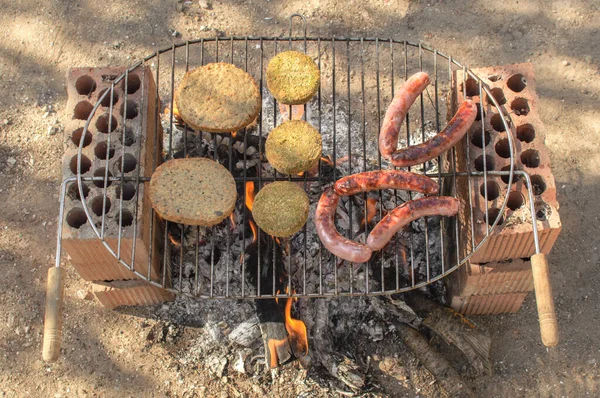 田舎の晴れた日にレンガで作られた素朴なバーベキューでハンバーガーとソーセージのトップビュー — ストック写真
