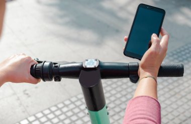 Modern şehir caddesinde dururken elektrikli scooter kiralamak için akıllı telefonu kullanan tanınmayan biri.