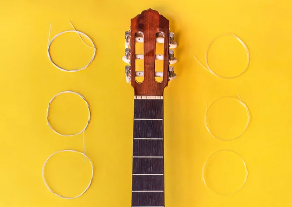 Changing the strings to a guitar: guitar neck without strings and new strings to put on the instrument isolated on yellow background. Luthier work.