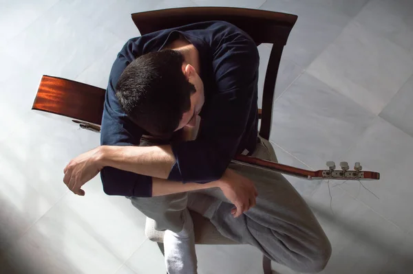 Sıkılmış ve ilham vermeyen gençler gitar çalmaya ara veriyor. Elinde gitarla dinlenen bir adamın üst görüntüsü. İlham ve motivasyon eksikliği kavramı.