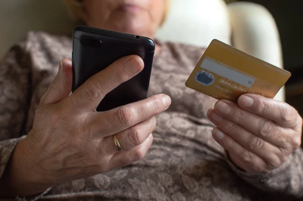 Evde kredi kartı ve akıllı telefon kullanan yaşlı bir kadın online alışveriş yapıyor. Yaşlılar, teknoloji ve internet kavramı...