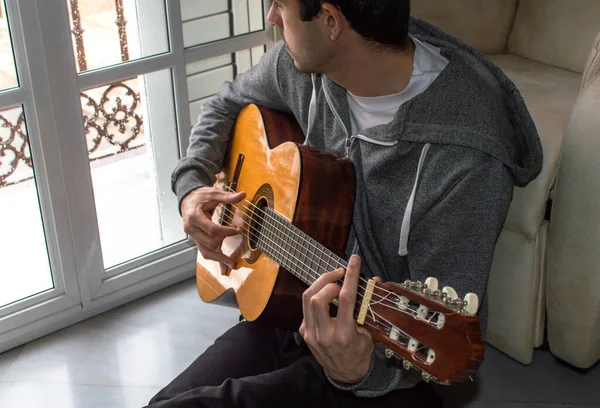 Melankolik genç adam fırtınalı bir günde gitar çalarken pencereden yağmuru izliyor..