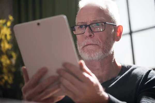 Senior man met zijn tablet, harde lichteffect — Stockfoto