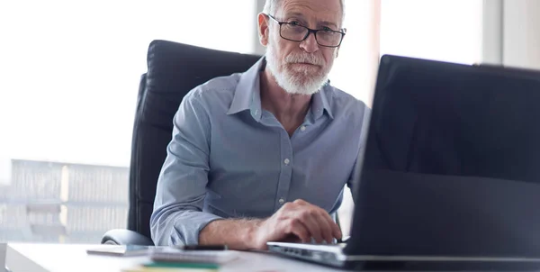 Portret van senior zakenman die op laptop, hard licht werkt — Stockfoto