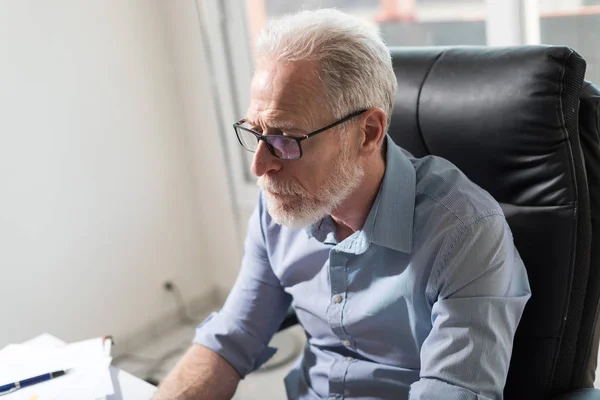 Senior affärsman sitter vid sitt skrivbord, hårt ljus — Stockfoto