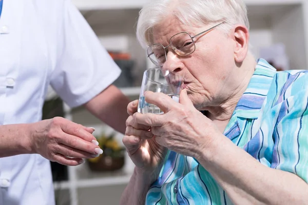 Enfermera dando vaso de agua a la mujer mayor — Foto de Stock