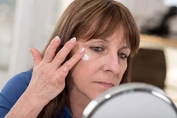 Woman putting anti-age cream on her face — Stock Photo, Image