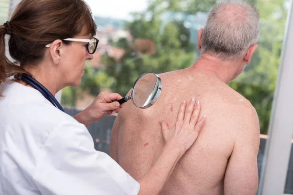 Dermatologista examinando a pele de um paciente — Fotografia de Stock