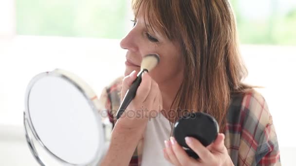 Зрелая женщина наносит макияж на лицо кисточкой — стоковое видео