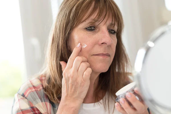 Mulher aplicando hidratante em seu rosto — Fotografia de Stock