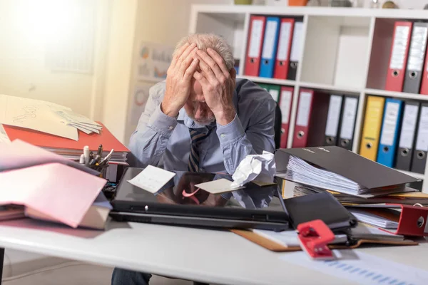 Überarbeiteter Geschäftsmann sitzt an einem chaotischen Schreibtisch, Lichteffekt — Stockfoto