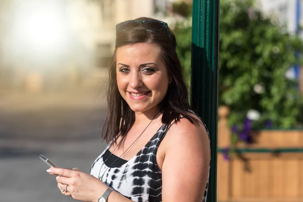 Pretty young woman holding her mobile phone in the street, light — Stock Photo, Image