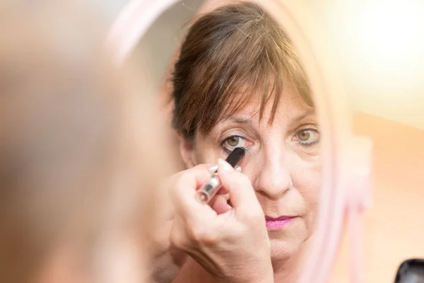 Senior woman applying eyeliner, light effect — Stock Photo, Image