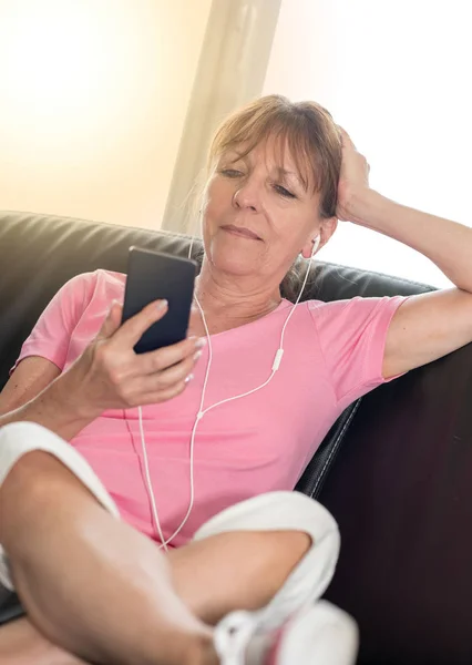 Femme assise sur le canapé et écoutant de la musique avec son téléphone portable — Photo