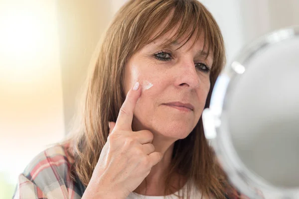 Mulher aplicando hidratante em seu rosto — Fotografia de Stock
