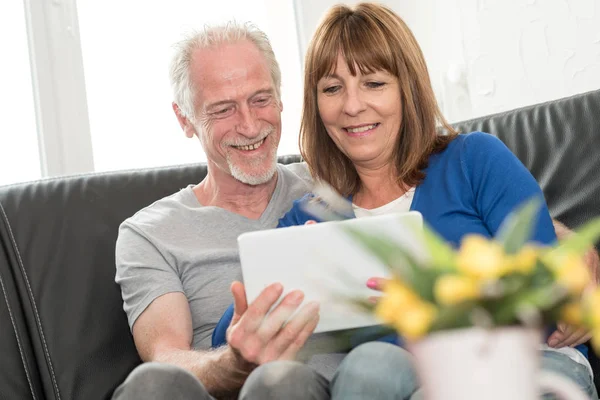 Couple mature moderne assis sur un canapé et utilisant une tablette — Photo