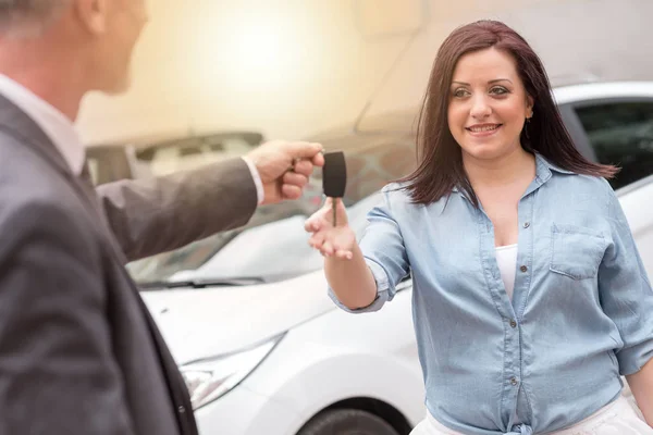 Carro vendedor entregando chaves do carro para a jovem mulher, efeito de luz — Fotografia de Stock