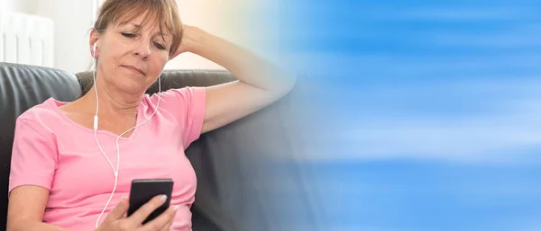 Femme assise sur le canapé et écoutant de la musique avec son téléphone portable — Photo