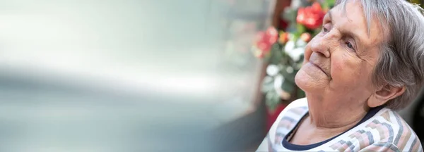 Elderly woman looking out the window; panoramic banner — Stock Photo, Image