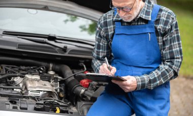 Araba tamircisi bir arabanın motorunu kontrol ediyor.