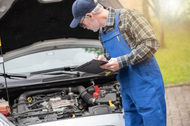 Araba tamircisi bir arabanın motorunu kontrol ediyor.