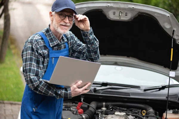 Mecânico usando laptop para verificar o motor do carro — Fotografia de Stock