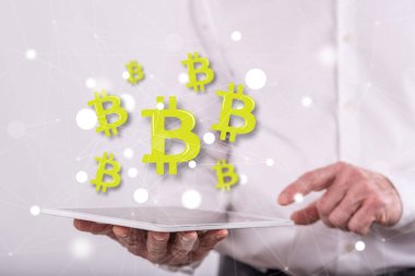 Arka planda bir adamın tuttuğu tabletin üzerinde Bitcoin kavramı