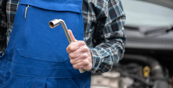 Car mechanic holding tools with car engine on background