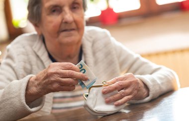 Yaşlı bir kadın cüzdanından bir banknot çıkarıyor.