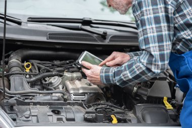 Car mechanic using digital tablet for checking car engine