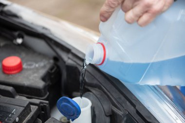 Mavi ön cam temizleme sıvısını arabaya döken tamircinin elleri.