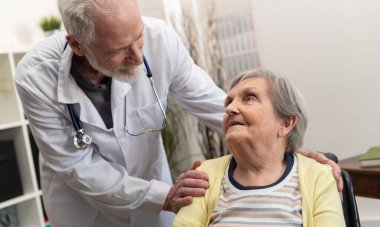 Erkek doktor huzurevindeki yaşlı kadına destek oluyor.