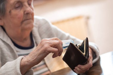 Yaşlı bir kadın cüzdanından bir banknot çıkarıyor.