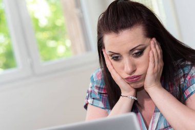 Dizüstü bilgisayarın önünde oturan çok çalışan genç iş kadını.