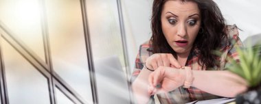 Stresli genç iş kadını saatine bakıyor.