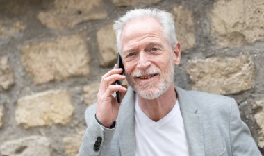 Olgun bir adam cep telefonunu açık havada kullanıyor.