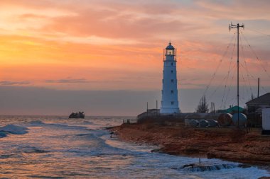 Cape 'de portakal rengi gün batımı. Resimli Tarkhankut deniz feneri, Kırım sahili ve arka planda batık bir gemi.