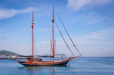 Yacht with lowered sails, blue sea, blue sky, seagulls, Islands in the background.