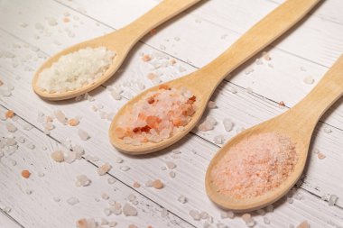 Beyaz ahşap bir masada tuzlu üç tahta kaşık Himalaya pembe tuzu büyük ve küçük beyaz deniz tuzu büyük.