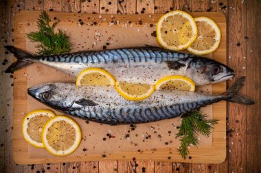 Baharat ve limonla marine edilmiş, otlarla süslenmiş kesme tahtasındaki kağıt üzerinde iki taze uskumru..