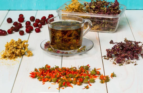 Tea from medicinal herbs. Dried medicinal herbs for health. Common meadow, oregano, marigold flowers, rosehip on a light wooden table. Blue wooden background.